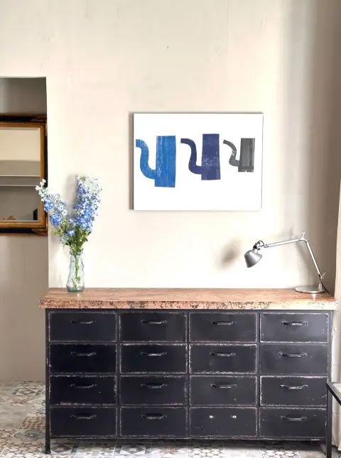 Zwart metalen ladenkast met een vaas blauwe delphinium onder een schilderij