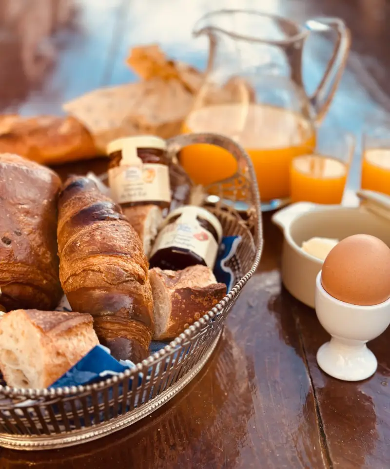 Ontbijt op tafel: stokbrood, croissants, een gekookt eitje, potjes jam uit de Dordogne en een kan verse jus